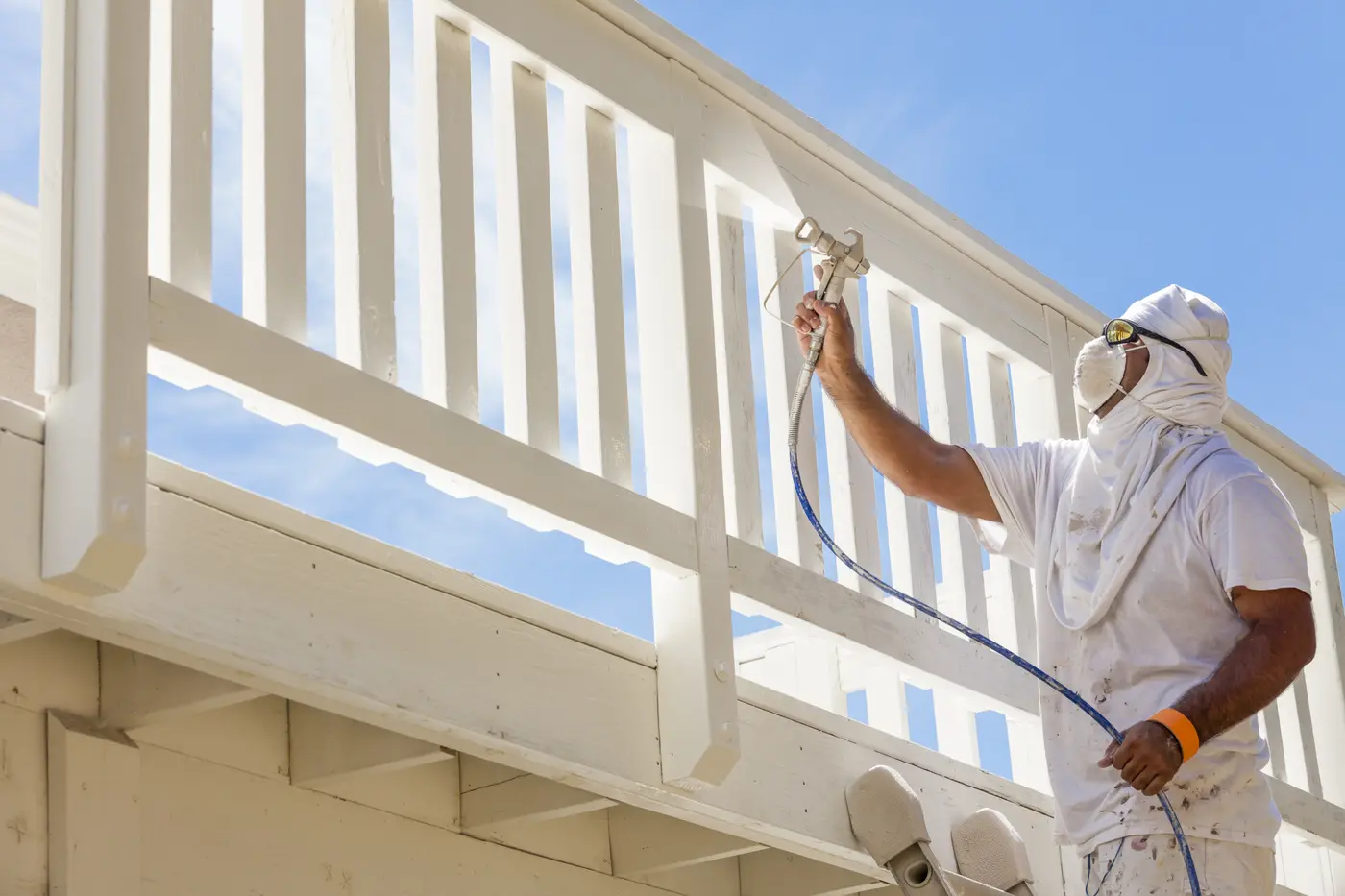 Painter spraying a white deck railing with an airless sprayer