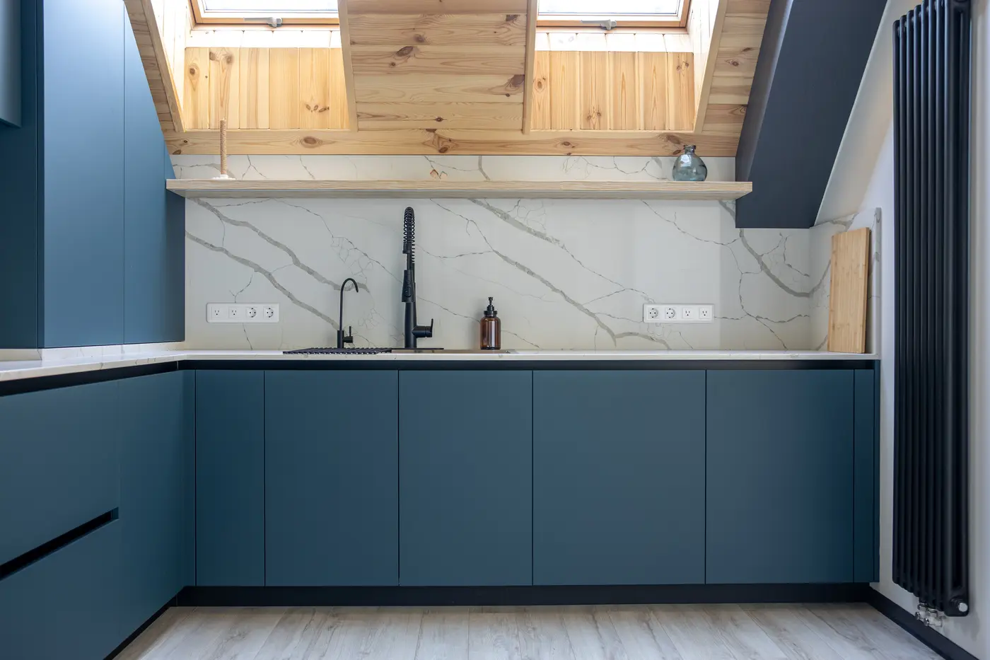 Matte blue lower cabinets beneath a white quartz backsplash and pine-paneled skylight