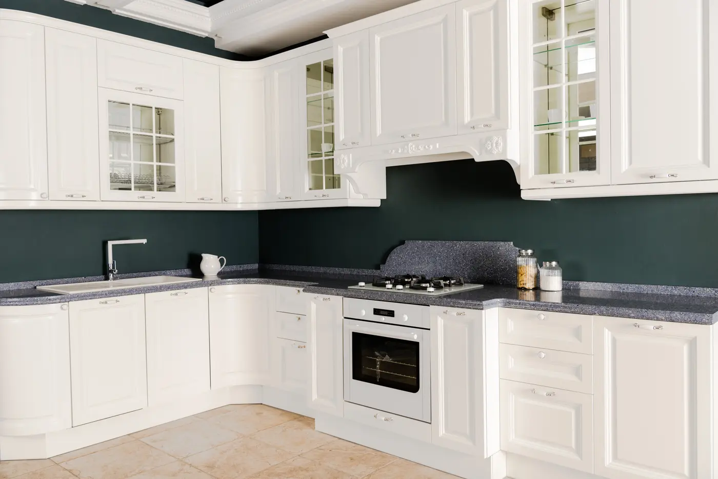 White raised-panel kitchen cabinets with glass-front uppers against dark green walls