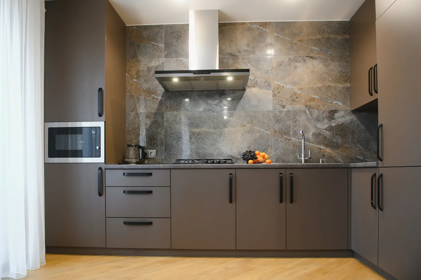 Taupe flat-panel kitchen cabinets with black pulls below a marble-look tile backsplash