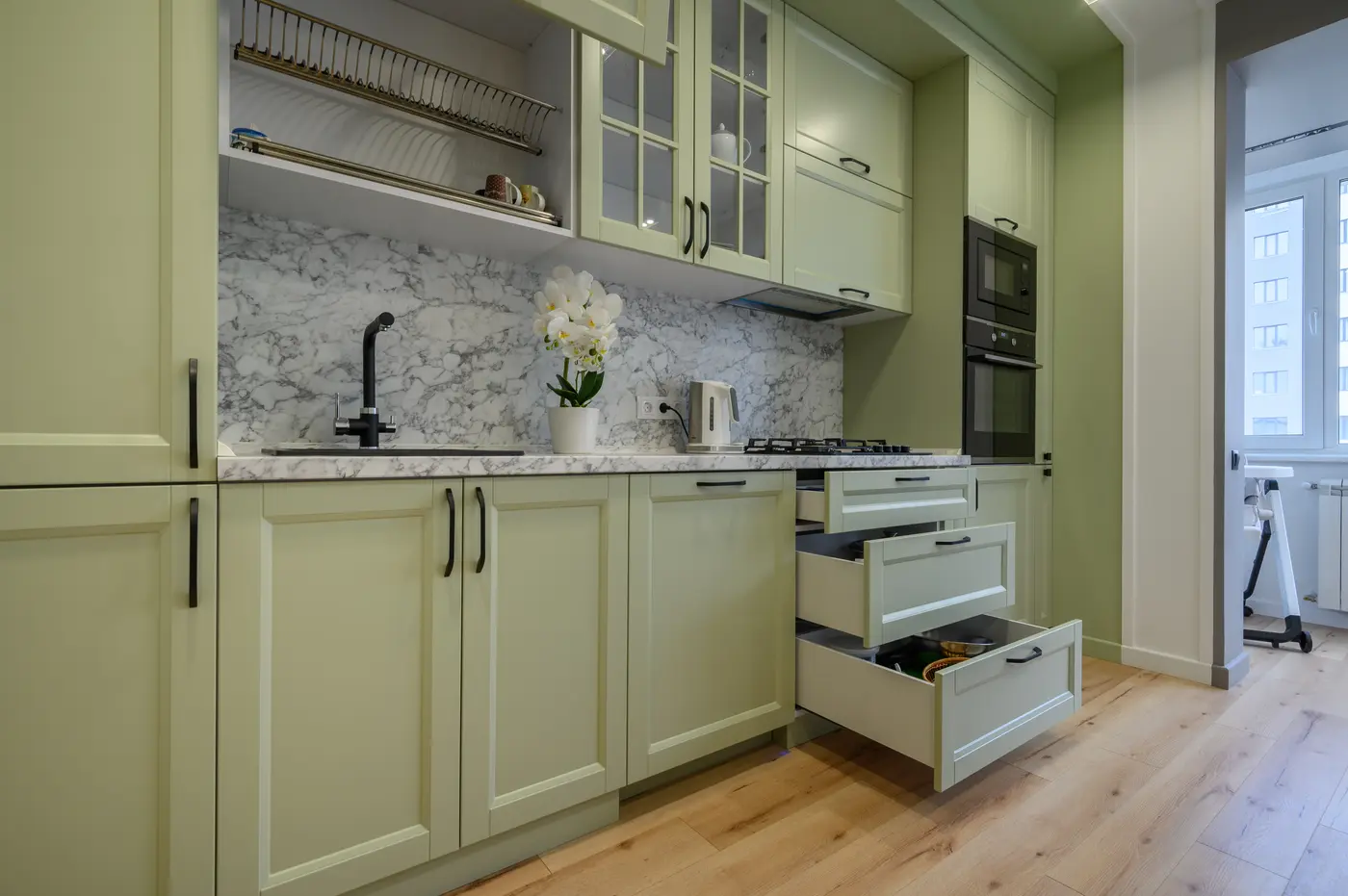 Sage green shaker kitchen cabinets with black pulls, marble backsplash and open drawers