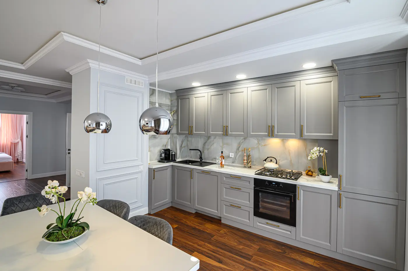 Gray shaker kitchen cabinets with brass pulls, marble backsplash and walnut floors