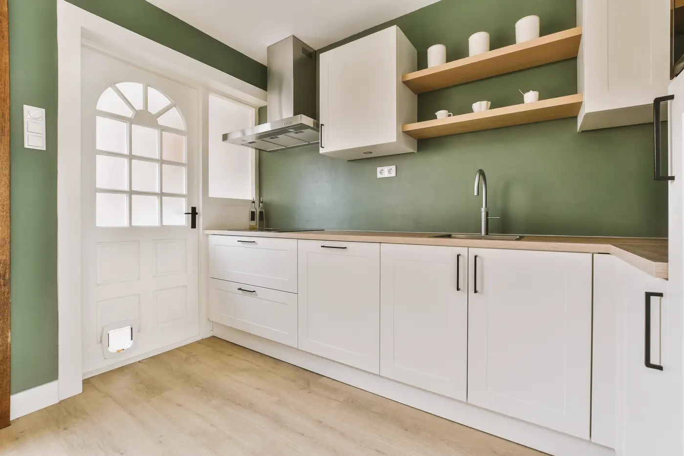 Sage green kitchen walls with white shaker cabinets and floating oak shelves