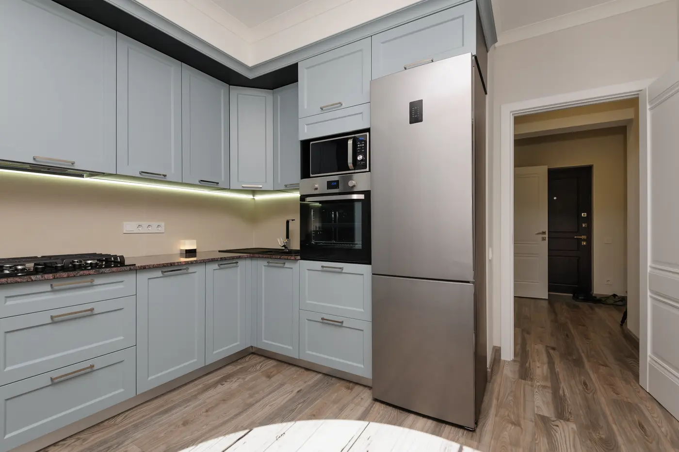 Light blue-gray shaker kitchen cabinets around a stainless fridge and built-in oven
