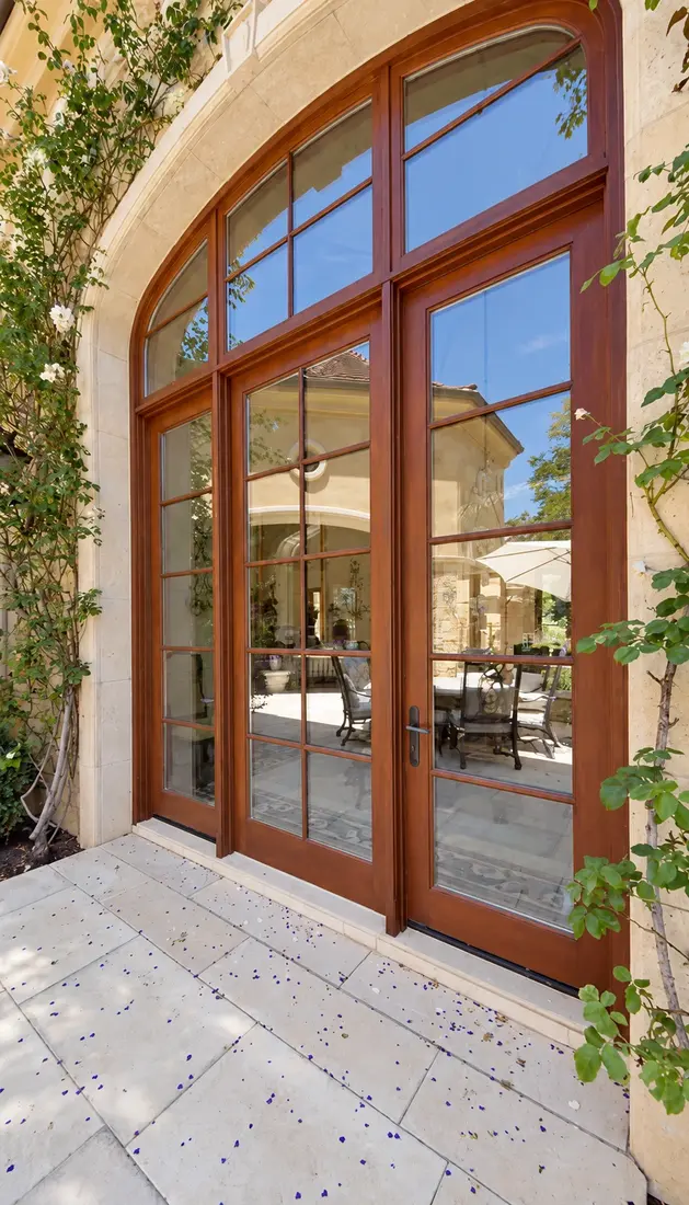Arched wood French doors with a transom, set in painted stucco and a stone surround