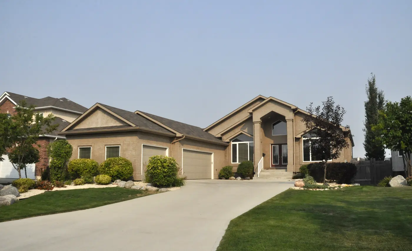 Single-story beige stucco home with a three-car garage, columned entry and green lawn