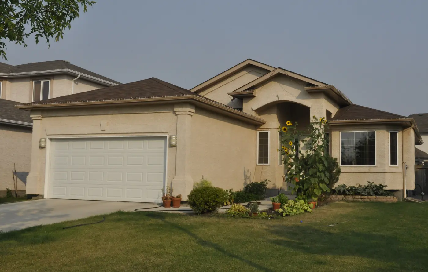 Single-story tan stucco home with a white two-car garage door and front lawn