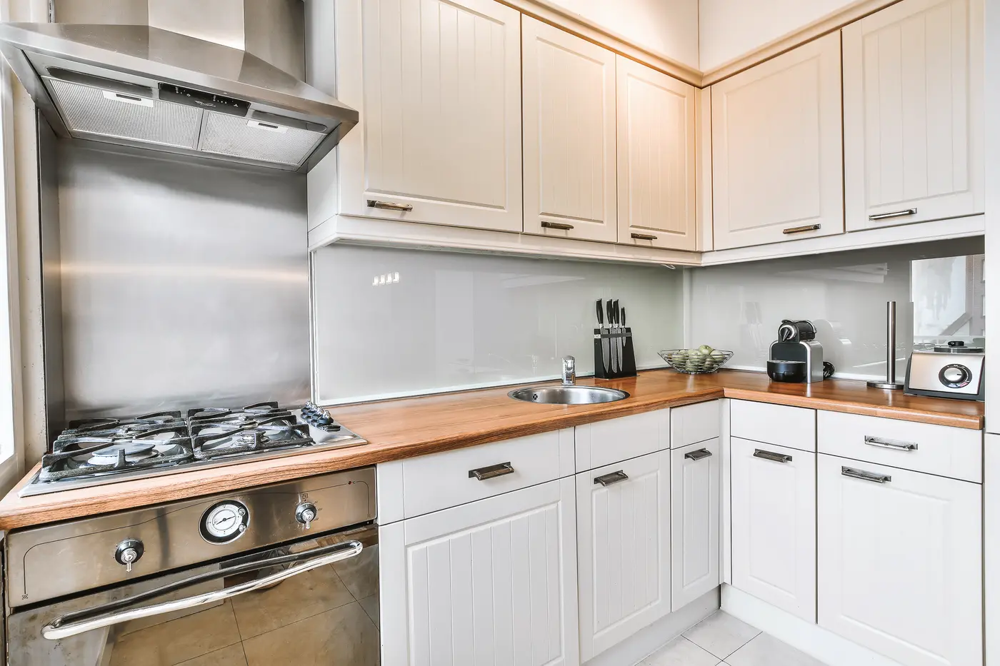 Cream beadboard kitchen cabinets with butcher-block counters and a stainless range
